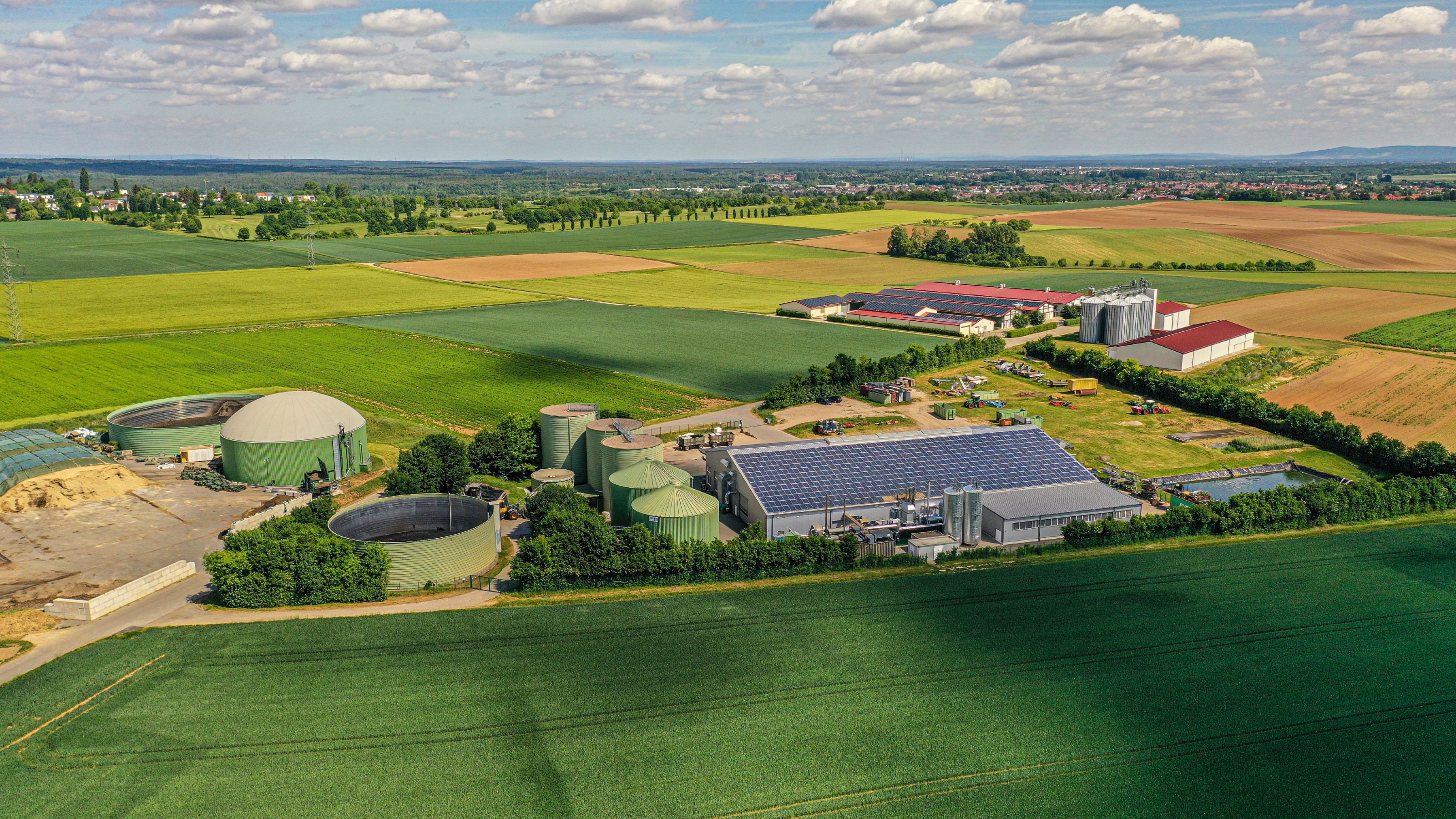 Vista aérea de una planta de biogás con varios digestores, depósitos y naves junto a una granja, rodeada de campos de cultivo